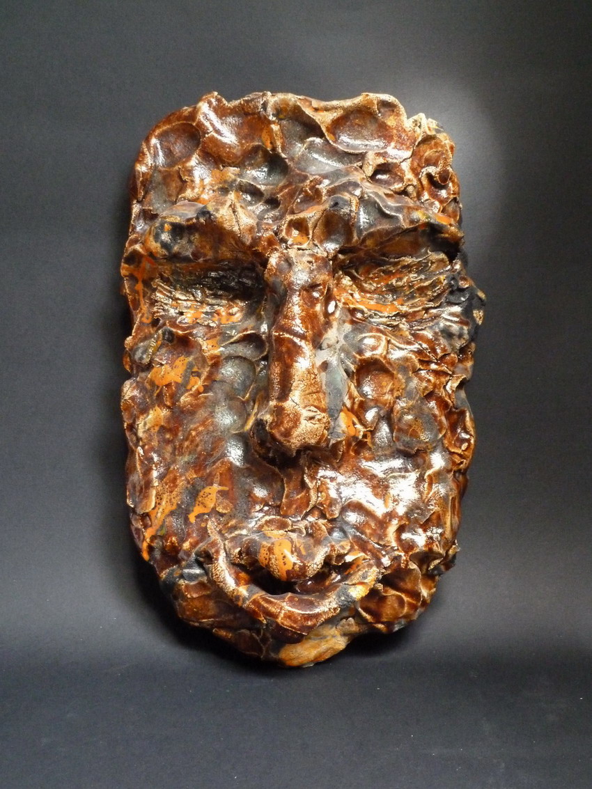 Scultura ceramica in tecnica raku che rappresenta un volto modellato con rilievi intensi e superfici irregolari, espressione di un’umanità in trasformazione.